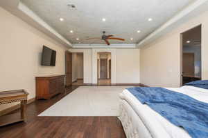 Bedroom with a tray ceiling, arched walkways, recessed lighting, dark wood-style floors, and ceiling fan