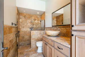 Full bath featuring tile walls, vanity, a shower stall, and stone tile flooring