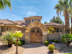 Mediterranean / spanish-style house with stucco siding, a gate, a tiled roof, and stone siding