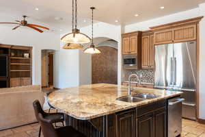 Kitchen featuring stone tile floors, arched walkways, open floor plan, stainless steel appliances, and recessed lighting