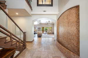 Foyer with arched walkways, stone tile floors, stairway, and ceiling fan