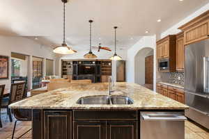 Kitchen with tasteful backsplash, a center island with sink, stone tile floors, light stone countertops, and recessed lighting