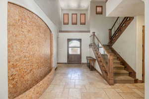 Foyer featuring stairway, a towering ceiling, stone tile floors, and arched walkways
