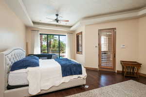 Bedroom with access to exterior, dark wood-type flooring, a ceiling fan, and a raised ceiling