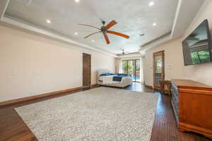 Bedroom featuring a tray ceiling, access to outside, dark wood-style flooring, recessed lighting, and a ceiling fan