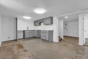 Kitchen with gray cabinetry, a textured ceiling, light countertops, and concrete floors