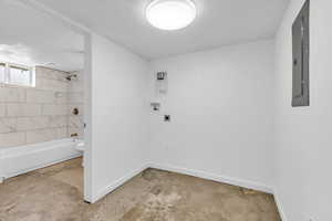 Bathroom with tub / shower combination, a textured ceiling, concrete floors, and electric panel