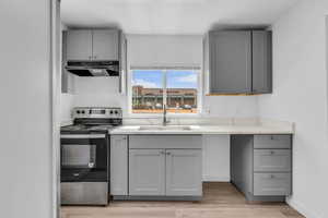Kitchen featuring gray cabinetry, stainless steel electric range, under cabinet range hood, and light wood-type flooring