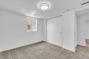 Unfurnished bedroom with light colored carpet, a textured ceiling, and a closet