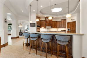 Kitchen featuring arched walkways, a breakfast bar area, pendant lighting, brown cabinets, and a tray ceiling