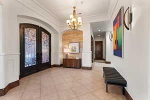 Entryway featuring french doors, arched walkways, light tile patterned floors, and a chandelier
