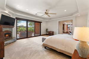 Carpeted bedroom featuring a tray ceiling, recessed lighting, access to exterior, ceiling fan, and a fireplace