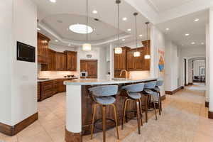 Kitchen with decorative backsplash, a tray ceiling, a breakfast bar area, pendant lighting, and recessed lighting