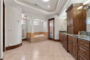 Bathroom featuring a bath, double vanity, light tile patterned floors, a tray ceiling, and recessed lighting