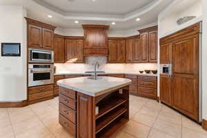 Kitchen featuring open shelves, built in appliances, light tile patterned flooring, a center island with sink, and tasteful backsplash