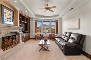 Living room with a premium fireplace, light colored carpet, a raised ceiling, built in shelves, and recessed lighting
