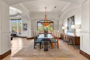 Dining room with light tile patterned flooring, arched walkways, a raised ceiling, and crown molding