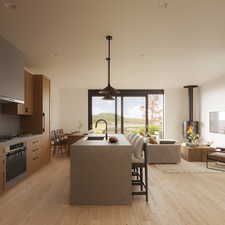 Kitchen featuring a wood stove, light wood-type flooring, light stone countertops, appliances with stainless steel finishes, and an island with sink