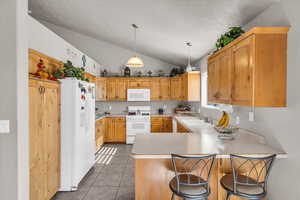 Kitchen featuring hanging light fixtures, a peninsula, white appliances, light countertops, and a breakfast bar area
