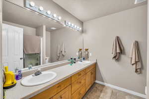 Full bathroom featuring double vanity, a textured ceiling, a shower stall, and light tile patterned floors