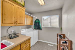 Laundry area with a textured ceiling, separate washer and dryer, cabinet space, and light tile patterned flooring