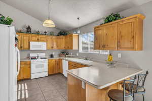 Kitchen featuring a kitchen bar, white appliances, a peninsula, decorative light fixtures, and light countertops