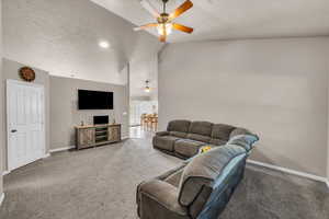 Carpeted living area featuring a textured ceiling, high vaulted ceiling, and ceiling fan