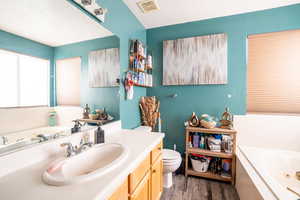 Full bathroom featuring a tub with jets, vanity, dark wood-style flooring, and a textured ceiling