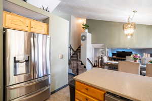 Kitchen with stainless steel refrigerator with ice dispenser, a chandelier, light brown cabinetry, open floor plan, and pendant lighting