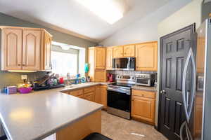 Kitchen featuring stainless steel appliances, light brown cabinetry, vaulted ceiling, a peninsula, and light countertops