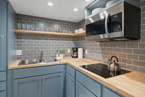 Kitchen featuring stainless steel microwave, open shelves, blue cabinets, backsplash, and recessed lighting