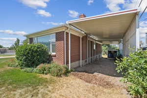 View of side of property with brick siding, a chimney, and an attached carport