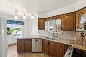 Kitchen featuring backsplash, light stone counters, dishwasher, light tile patterned floors, and a peninsula