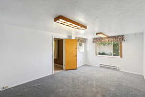 Carpeted spare room with a textured ceiling and a baseboard heating unit