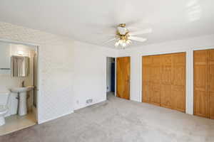 Unfurnished bedroom with two closets, carpet floors, ceiling fan, connected bathroom, and wallpapered walls