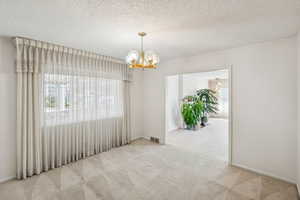 Spare room with carpet floors, a textured ceiling, and a chandelier