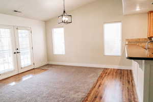 Unfurnished dining area with healthy amount of natural light, french doors, light wood-style floors, and vaulted ceiling