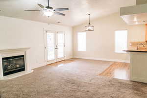 Unfurnished living room with french doors, vaulted ceiling, light colored carpet, a glass covered fireplace, and ceiling fan