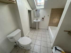 Full bath featuring light tile patterned floors, a skylight, a tub to relax in, and a textured wall