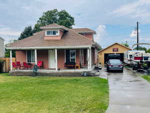 View of front facade featuring a shingled roof, driveway, a porch, and an outbuilding
