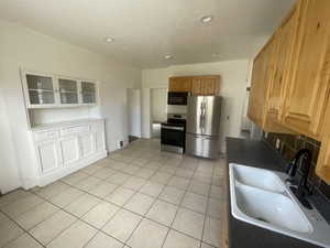 Kitchen with appliances with stainless steel finishes, light tile patterned flooring, a textured ceiling, decorative backsplash, and dark countertops