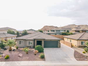 View of front of home featuring an attached garage, stone siding, concrete driveway, a residential view, and stucco siding