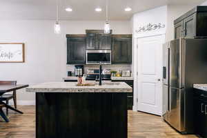 Kitchen featuring a kitchen island with sink, appliances with stainless steel finishes, hanging light fixtures, light wood-type flooring, and recessed lighting