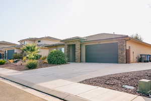Prairie-style home featuring driveway, stucco siding, an attached garage, and stone siding