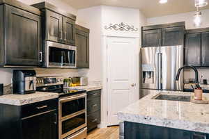 Kitchen with appliances with stainless steel finishes, light wood-type flooring, decorative light fixtures, dark brown cabinetry, and recessed lighting