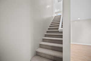 Staircase with wood finished floors and recessed lighting