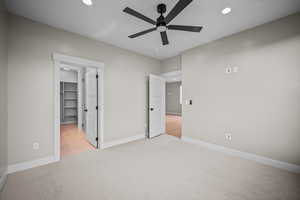 Unfurnished bedroom featuring light carpet, a walk in closet, recessed lighting, and ceiling fan