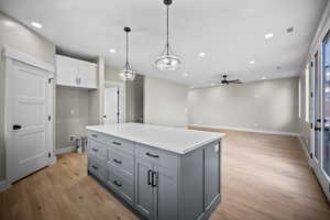 Kitchen with hanging light fixtures, gray cabinetry, a kitchen island, white cabinets, and light wood finished floors