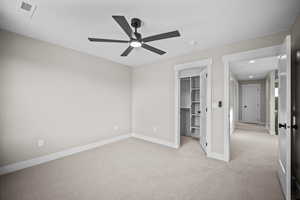 Unfurnished bedroom featuring carpet, a walk in closet, and a ceiling fan