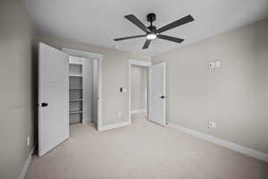 Unfurnished bedroom with light carpet, a walk in closet, and ceiling fan